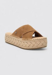 Sandalias de slide de ante marrón con tiras cruzadas y suela de plataforma de yute trenzado. La plantilla es beige y se puede ver un pequeño detalle de logo en la tira.
