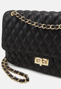 Černá prošívaná kožená kabelka se zlatým řetězovým popruhem a kováním. Má obdélníkový tvar a výrazné zlaté zapínání na klips.