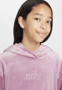 Lila aksamitna kapuca z nevsiljivim "nike" logotipom. Ima sproščen kroj, širok ovratnik in mehak občutek.