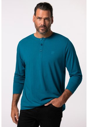 Teal langemouwen henley shirt gemaakt van zacht materiaal, met een drieknoopssluiting en een subtiele reliëflogo op de borst.