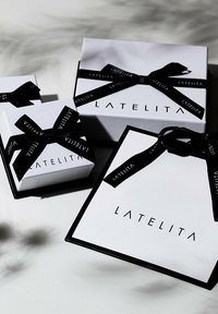 Tre vita presentförpackningar med svarta detaljer, med svarta satinband och ordet "LATELITA" tryckt med fet svart stil på varje låda.