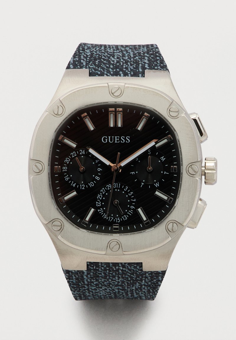Ανδρικό ρολόι Guess με μαύρο καντράν με υφή, ασημένια δείκτες, υποκαντράν για ημερομηνία και ημέρα, ασημένιο στεφάνι με εμφανείς βίδες και λουράκι από υφασμάτινο μοτίβο.