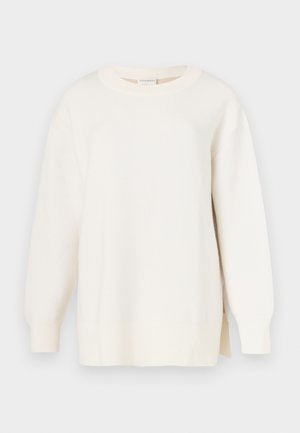 Krém színű pulóver texturált kötött mintával, kerek nyakkivágással és enyhén oversized fazonnal. Hosszú ujjakkal és oldalsó sliccel a szegélyén.