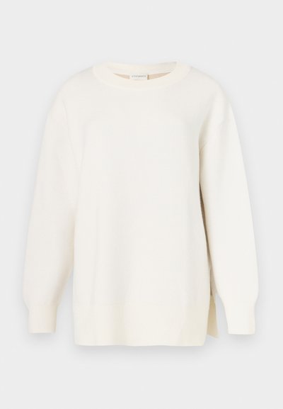 Pulover de culoare crem cu țesătură texturată, decolteu rotund și croială ușor oversized. Are mâneci lungi și șlițuri laterale la tiv.