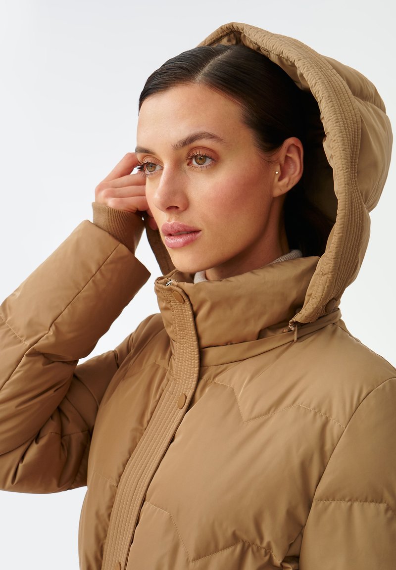 Brązowa kurtka puchowa z kapturem, teksturowany materiał, zamek błyskawiczny z przodu oraz ściągacze na mankietach. Posiada przeszycia na ramionach.