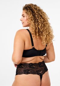 Reggiseno in pizzo nero con spalline regolabili, caratterizzato da una fascia liscia e dettagli in pizzo floreale. Abbinato a slip con bordi in pizzo coordinati.