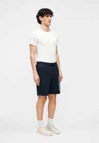 Biele tričko s krátkym rukávom a tmavomodré šortky s potlačou loga. Šortky majú elastický pás a sú vyrobené z mäkkého materiálu.