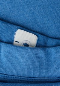 Blåt sweatshirtstof lagdelt, med en ribstrikket halsudskæring og en hvid etiket med en klar knap til fastgørelse.