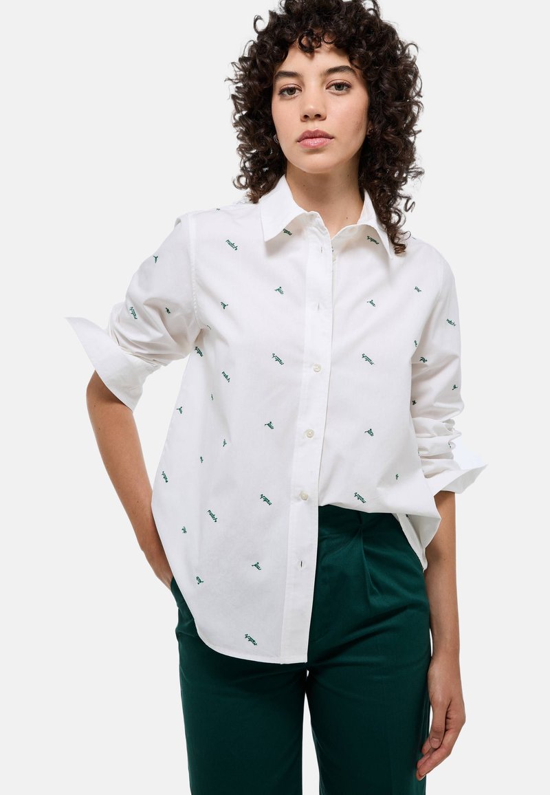 Chemise blanche à boutons avec des détails brodés verts, manches longues retroussées, associée à un pantalon vert. Comprend un col classique et une fermeture à boutons.