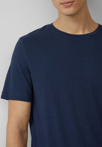 Marineblaues T-Shirt mit kurzen Ärmeln aus weichem Baumwollstoff, das über einen klassischen Rundhalsausschnitt und eine glatte Textur verfügt.