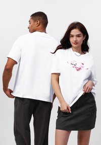Hvide kortærmede t-shirts med et pink grafisk design foran, parret med mørke jeans og en sort denimnederdel.