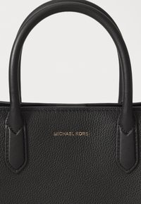 Sac à main noir en cuir texturé avec des poignées arrondies et un petit logo doré Michael Kors centré sur le panneau avant.