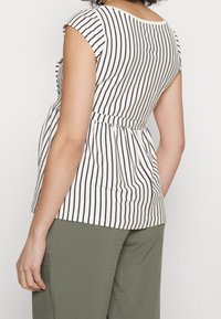 Pruhovaná blůza s kulatým výstřihem a krátkými rukávy. Bílá látka je zdobena námořnickými svislými pruhy a je stažena v pase pro lepší střih.