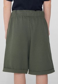 Shorts vert kaki avec une finition texturée, dotés d'une taille élastique et de poches roulées, conçus pour le confort et la liberté de mouvement.