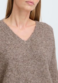 V-neck sweater made of soft brown textured knit fabric, featuring a relaxed fit and ribbed neckline detail.