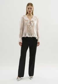 Lichtroze blouse met een gekruide halslijn en mouwboorden, gestructureerde stof, gelaagde zoom, gecombineerd met zwarte broek en zilveren flats.