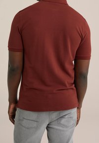 Mörkröd polo med texturerad tyg och korta ärmar, matchad med ljusgrå jeans med bakfickor. Rent design, enhetliga färger.