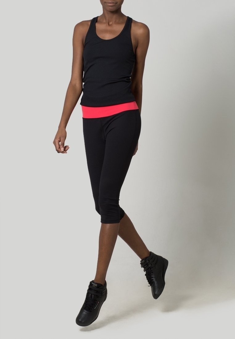 Débardeur noir sans manches avec une ceinture rose, associé à des leggings capri noirs et des chaussures de sport noires à lacets. Texture de tissu lisse.