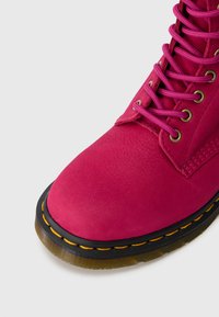 Bottines en suédine rose vif, bout rond, à lacets sur le devant, avec œillets dorés et semelle en caoutchouc noir ornée de surpiqûres orange.