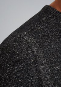 Dunkelgrauer Strickpullover mit einem strukturierten Muster. Nahaufnahme der Schulternaht, die ein dezentes, gemischtes Garn-Detail und einen gerippten Halsausschnitt zeigt.