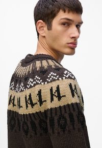 Pletena dukserica s geometrijskim uzorkom u smeđoj, bež i crnoj boji, s kružnim izrezom i teksturiranim detaljima na tkanini.