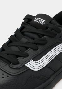 Black leather sneaker with white accents, featuring round laces, a padded collar, and a rubber sole. The brand logo is visible on the tongue.