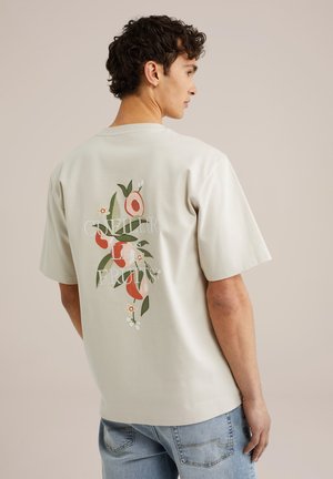 Lys beige t-shirt med korte ærmer, der har et blomstermotiv med røde frugter og grønne blade. Grafikken inkluderer tekst i hvid. Casual pasform.