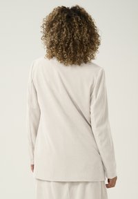 Top in corda beige a maniche lunghe con righe verticali e un fit rilassato, caratterizzato da un orlo leggermente arrotondato e una texture sottile.