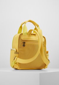 Mochila amarilla con tejido texturizado y acentos suaves. Cuenta con correas ajustables, un bolsillo con cremallera y un detalle tejido en el costado.