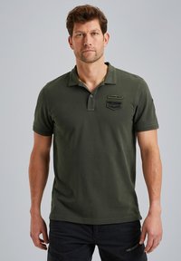 Polo de color verde oliva hecho de algodón, con una tapeta de tres botones, parches bordados y mangas cortas con puños de canalé.