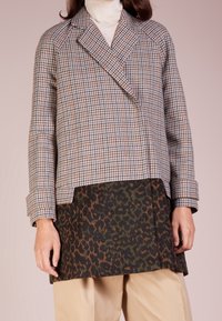 Dobbeltradet frakke med hundetandsmønster i beige og brun, med en kontrasterende mørkegrøn og brun leopardprint nederste sektion.