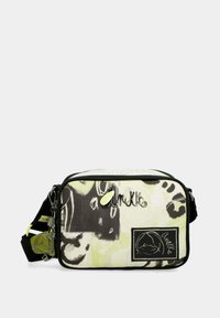 Bolso bandolera de tela con un patrón abstracto en blanco y negro, que presenta un logo prominente, cierre de cremallera y un charm desmontable.