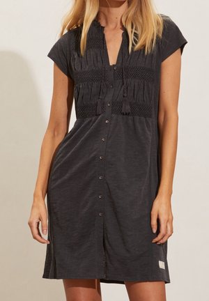 Dunkelgraues, kurzärmliges Kleid aus weichem Stoff, mit einem gerafften Oberteil, Knopfleiste und seitlichen Schlitzen. Enthält Quasten-Details.