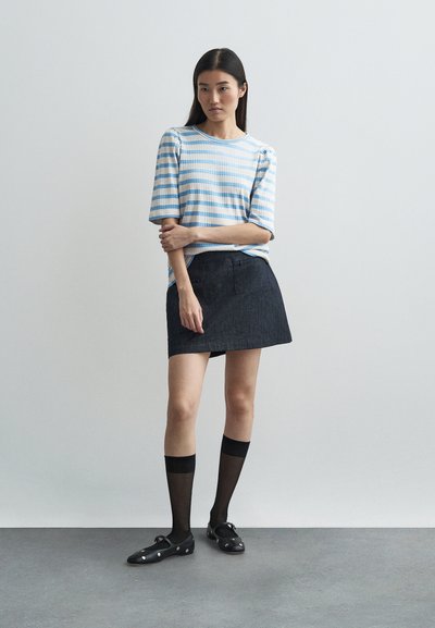 Ριγέ μπλε και άσπρη μπλούζα κοντομάνικη, μαύρη τζιν μίνι φούστα, μαύρες κάλτσες έως το γόνατο και μαύρα παπούτσια με ασημί λεπτομέρειες.