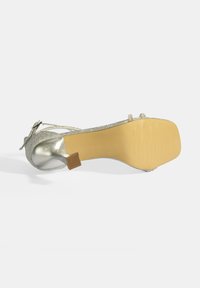Zilveren glinsterende hoge hak met een ronde teen, dunne hak, flexibele zool en decoratieve banden. Gladde metallic afwerking op de hak.