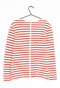 Maglietta a maniche lunghe a righe rosse e bianche con scollatura rotonda, spacchi laterali e tessuto a maglia testurizzato. Appesa a un gancio nero.