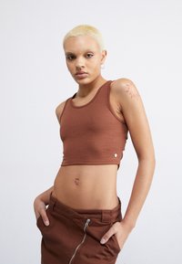 Top corto de canalé marrón con escote redondeado y detalle lateral, combinado con una falda marrón a juego con un zipper visible.