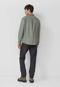 Groen shirt met lange mouwen, een button-down kraag en een plooi aan de achterkant, gecombineerd met donkerblauwe spijkerbroek en bruine enkellaarsjes.