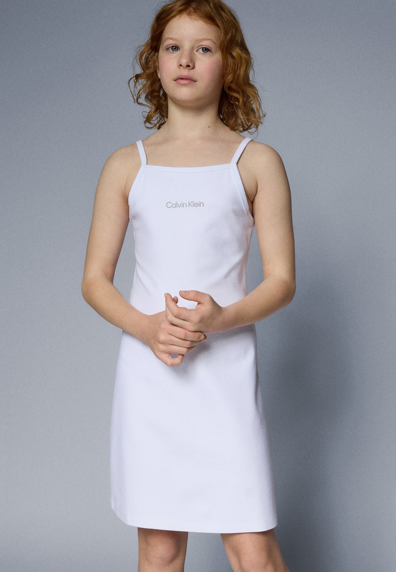 Robe blanche sans manches avec une coupe droite, fabriquée dans un tissu lisse. Elle présente des bretelles fines et un petit logo centré de "Calvin Klein".