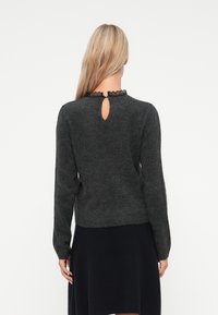 Mørkegrå genser med en teksturert finish, med lange ermer, en nøkkelhullåpning bak, og en blonder trim rundt halsen.