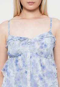 Lichtblauwe bloemenblouse van doorschijnende stof, met gerimpelde schouderbanden, knoopsluiting aan de voorkant en een ontspannen pasvorm met subtiele bloemenpatronen.
