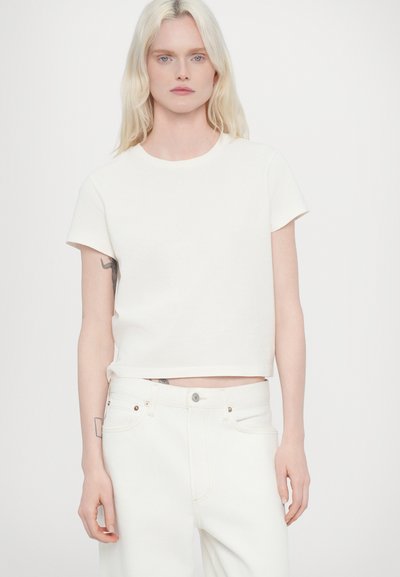 T-shirt blanc court en coton, avec un col rond et des manches courtes, associé à un jean blanc taille haute.