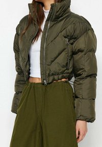 Olivově zelená krátká prošívaná bunda s vysokým límcem, zapínáním na zip a předními kapsami. Má prošívanou strukturu a elastický lem.