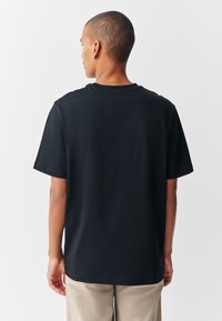 Juoda trumpomis rankovėmis marškinėliai iš minkštos medvilnės, laisvo silueto ir apvalia kaklo linija, matomi iš nugaros be matomų raštų ar akcentų.