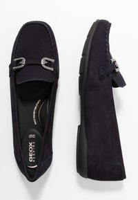 Marineblaue Wildleder-Slipper mit silberfarbenen Hardware-Akzenten, abgerundetem Zehenbereich, gesteppten Details und einer flexiblen schwarzen Gummisohle.