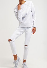 Ljusgrå sweatshirt med ribbad halsringning, kompletterad med vita slitna skinny jeans och grå sneakers med mesh-detaljer.