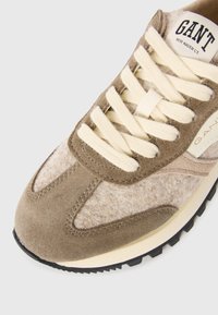 Beige och taupe sneakers med gräddfärgade snören, mocka- och ulltexturer, synlig svart sula, och etikett med "GANT New Haven CT." på tungan.