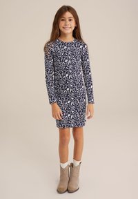 Marineblaues langärmeliges Kleid mit weißem Blumenmuster, Rundhalsausschnitt und Länge über dem Knie. Kombiniert mit hellbraunen Knöchelstiefeln.