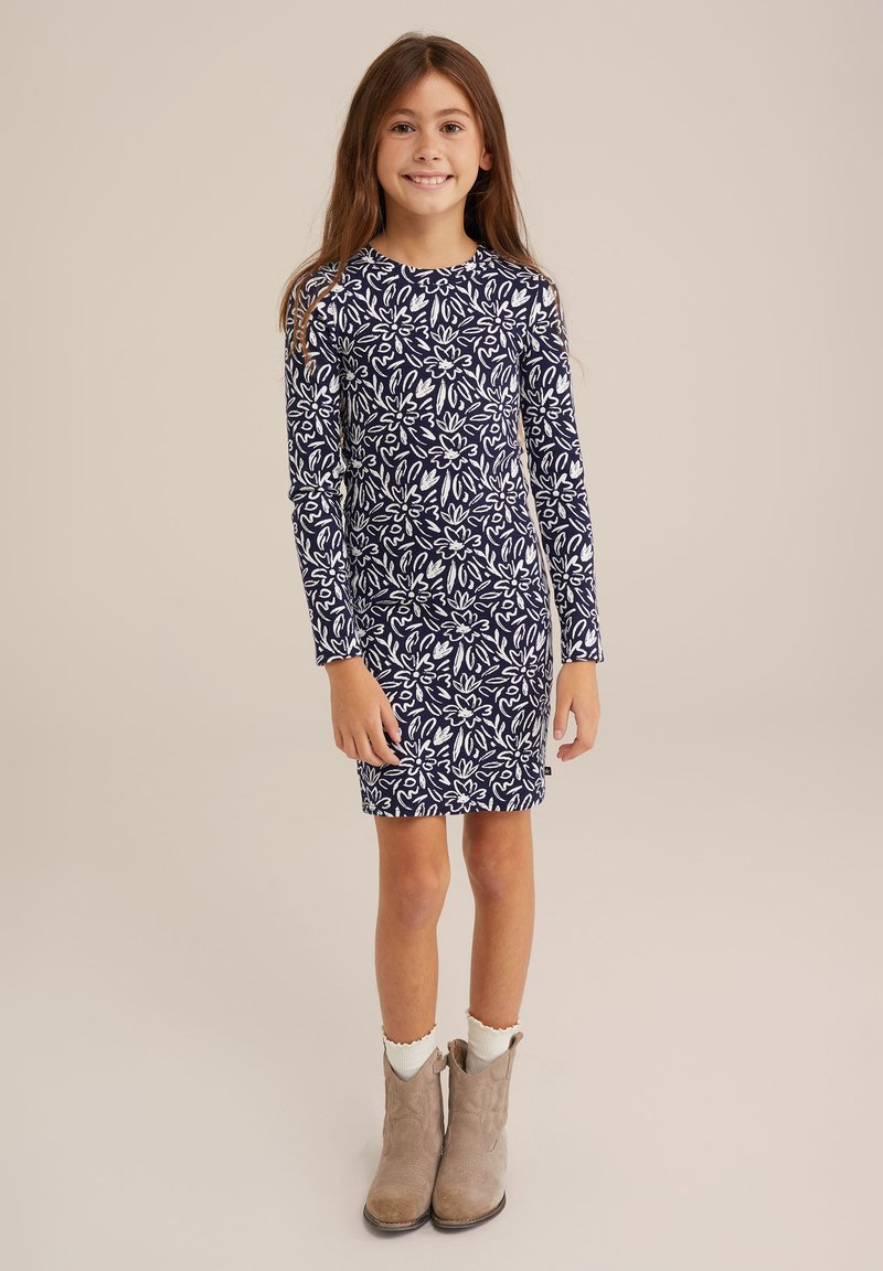 Marineblaues langärmeliges Kleid mit weißem Blumenmuster, Rundhalsausschnitt und Länge über dem Knie. Kombiniert mit hellbraunen Knöchelstiefeln.