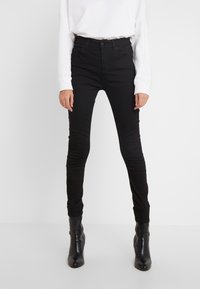 Jeans ajustados de tiro alto en color negro, fabricados en denim con una textura suave. Cuentan con un cierre de botón en la parte frontal y bolsillos traseros, combinados con botas negras.